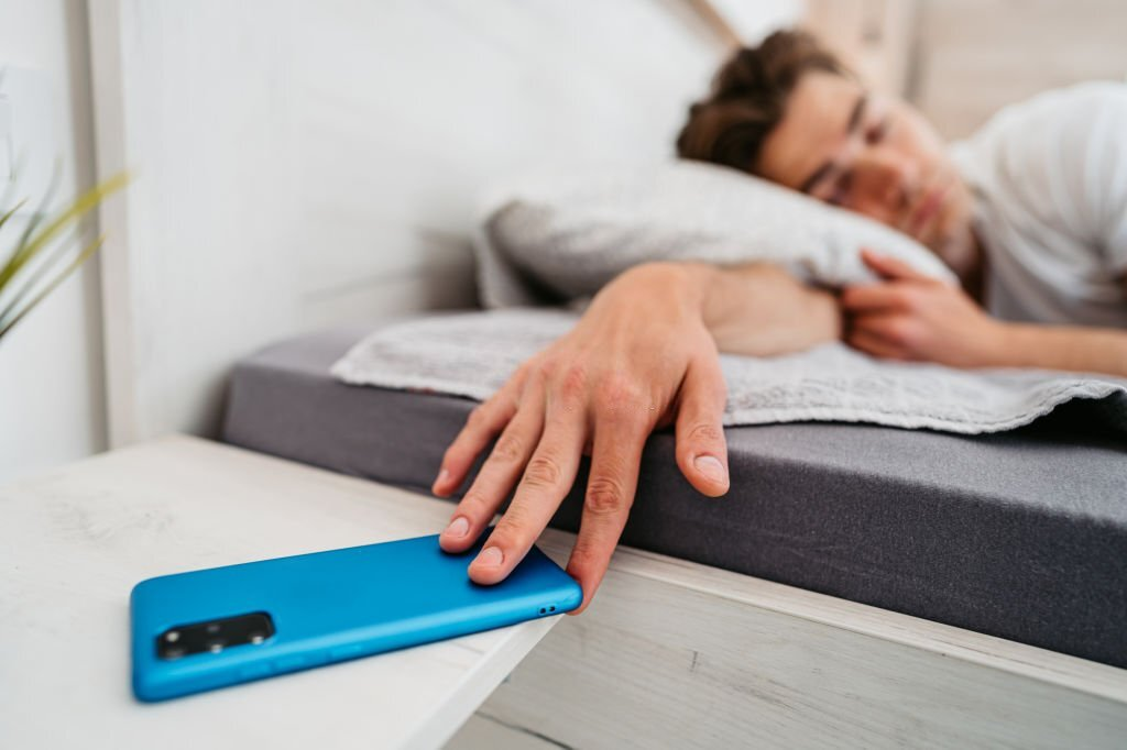 man snoozing the morning alarm, sleeping in